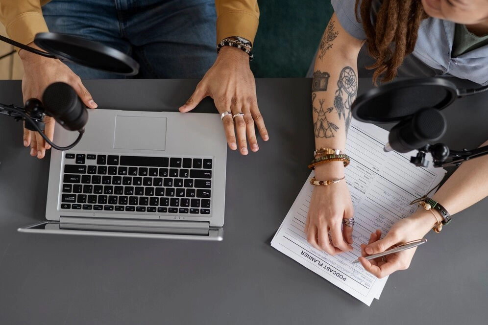 two people conversing, one with mic and laptop, one with paper and pen
-content creation services