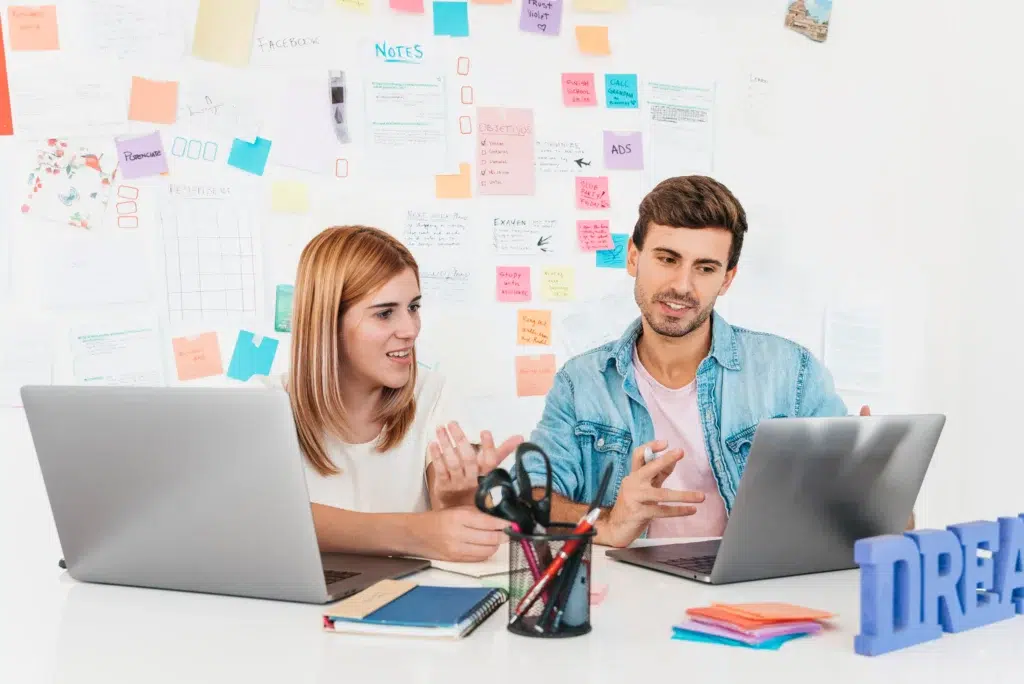 smiling-male-female-sitting-desk-talking-looking-laptop