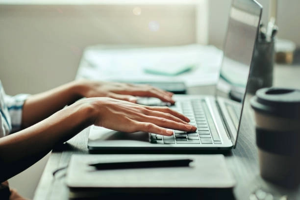 Hands typing on a laptop at a desk with a notebook. -content creation companies