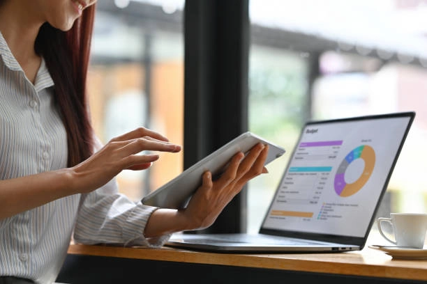 A person using both a tablet and a laptop to analyze a financial budget pie chart, emphasizing digital tools for financial management. -different types of marketing